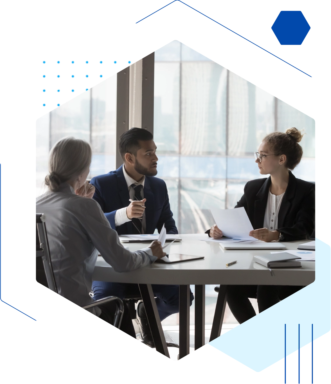 Three people in a business meeting sit at a table, discussing and reviewing documents in a modern office setting.