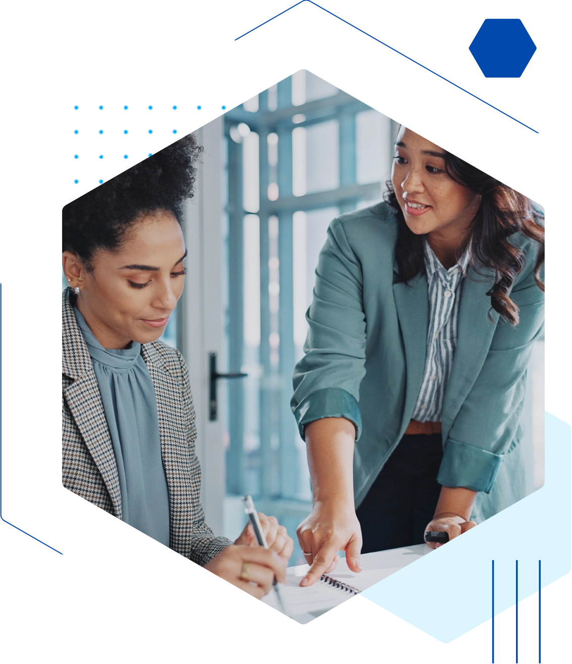 Two people in business attire collaborate at a table, with one person pointing at a document and the other taking notes.