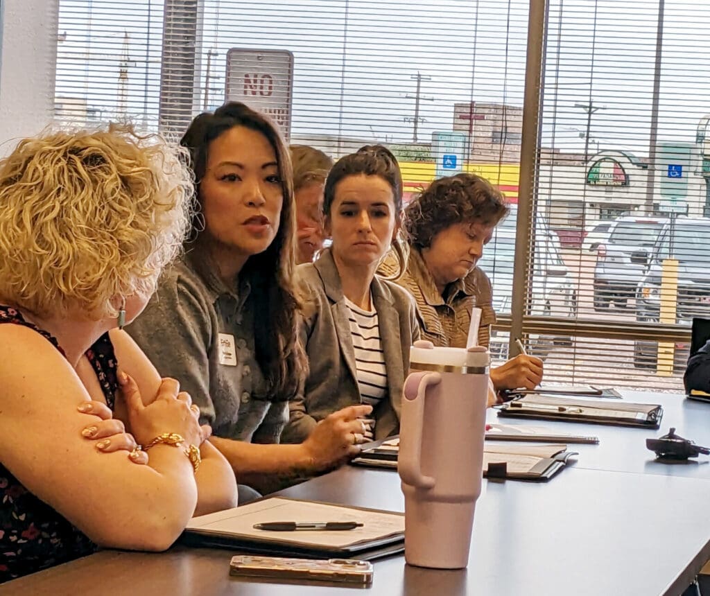 A Group Of People Sitting By A Desk